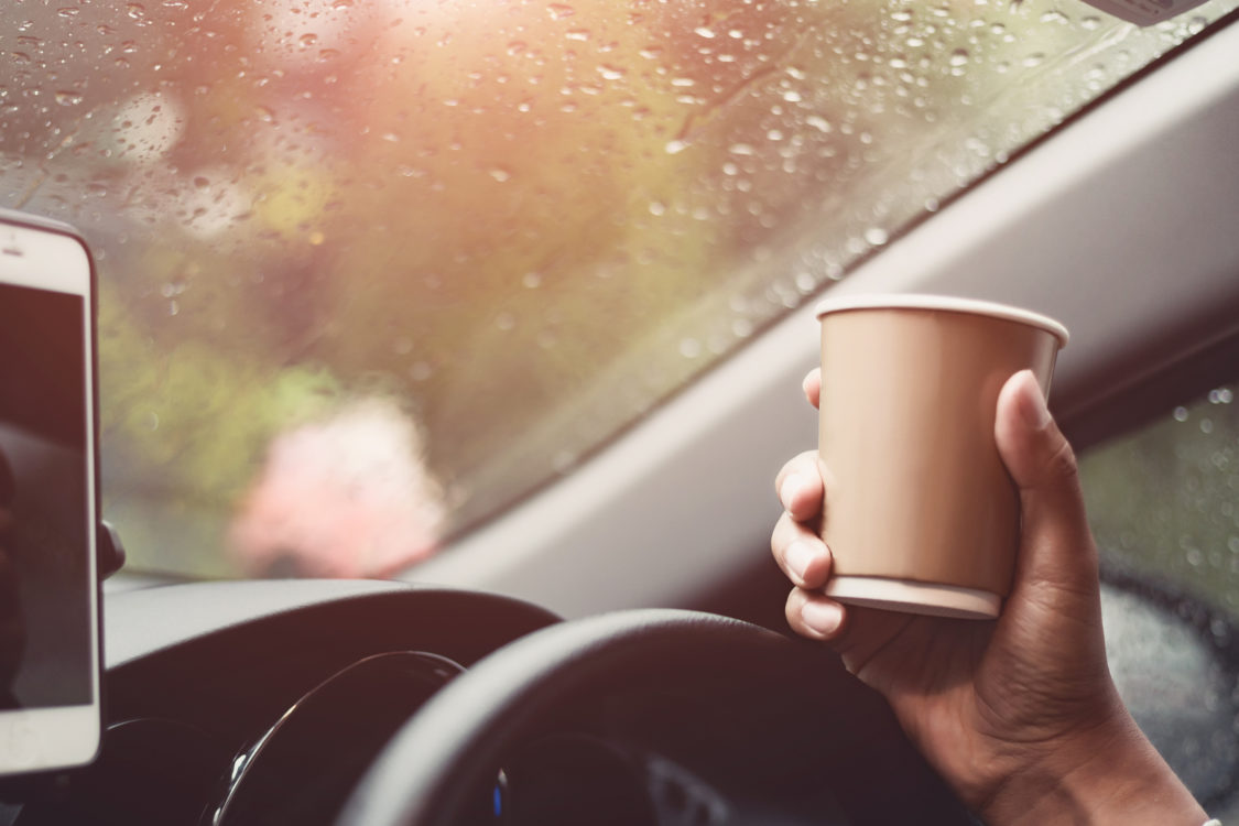 transportation and vehicle concept - driver drinking coffee while driving the car