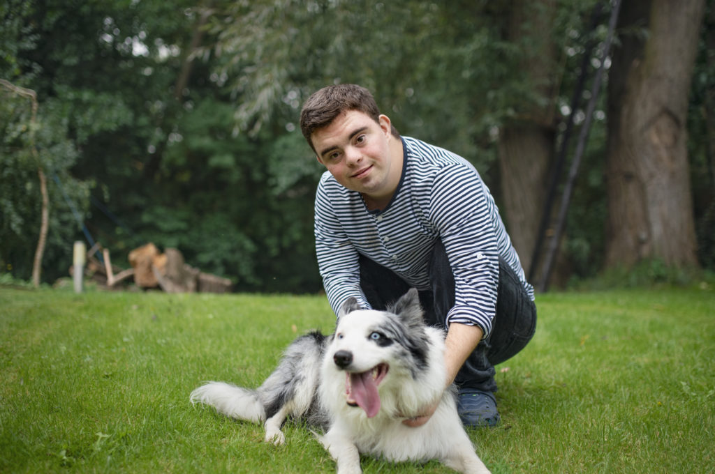 Portrait of cheerful down syndrome adult man playing with dog pet outdoors in backyard.
