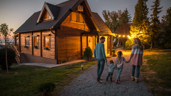 Rear view of happy family holding hands and walking by their chalet in the evening.