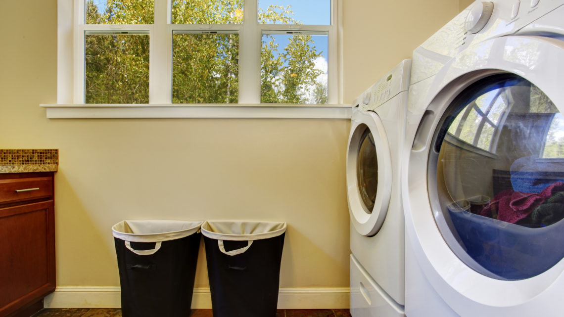 Bright laundry room with white modern appliances and black laundry baskets.