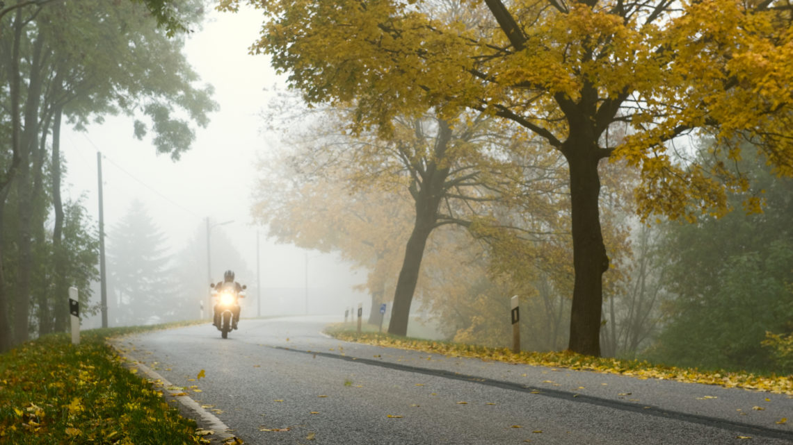 Single motorcycle rider driving bike down road on a foggy autumn morning