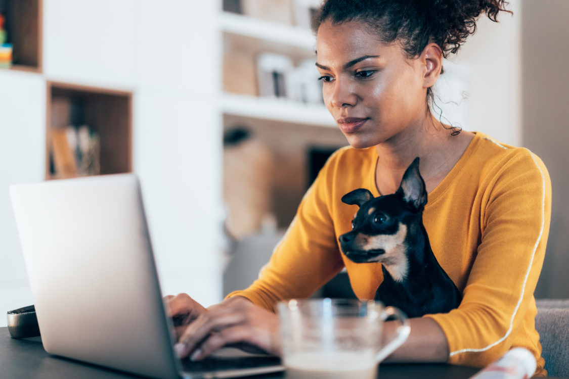 Jeune femme afro-américaine assise avec son chien et utilisant un ordinateur portable à la maison
