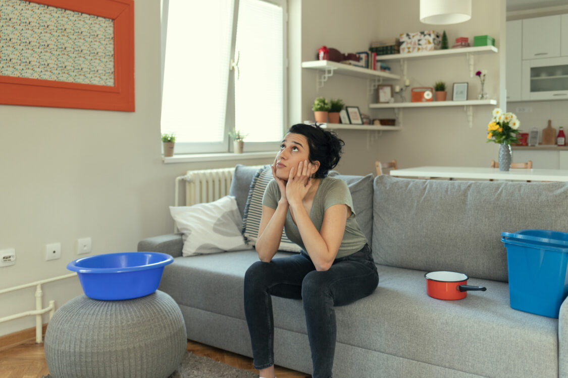Woman sitting in her living room watching water leak from the roof and into a bucket 