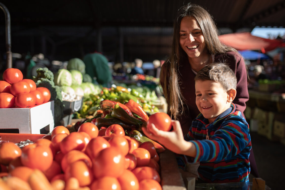 Un garçon cueille des légumes avec sa mère au marché fermier