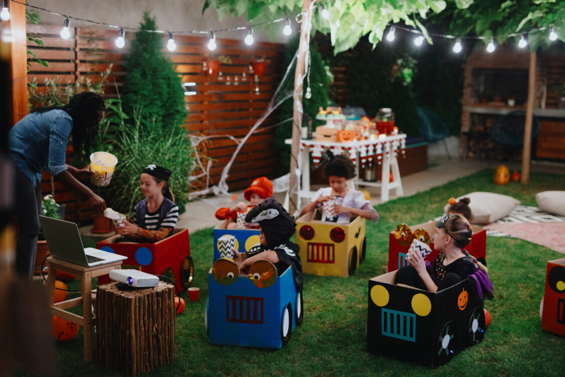 Groupe d'enfants lors d'une soirée cinéma dans le jardin. Assis dans des voitures en carton, mangeant du pop-corn et regardant un film.