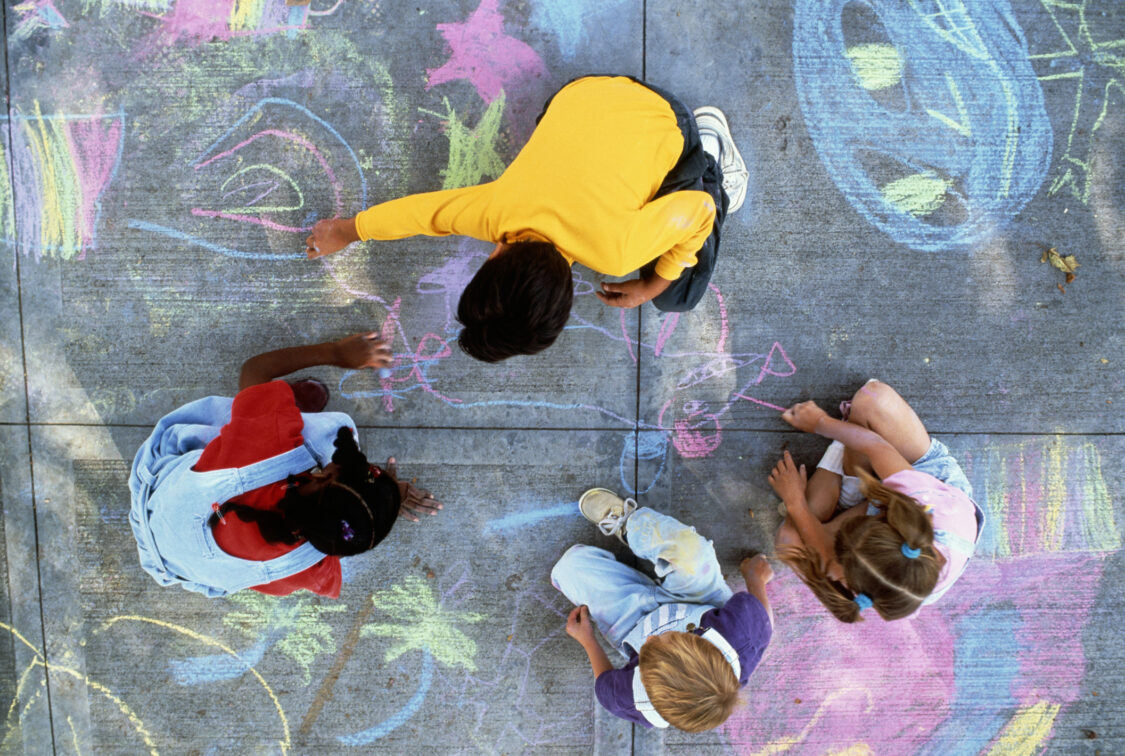 Four children drawing with chalk on pavement, overhead view