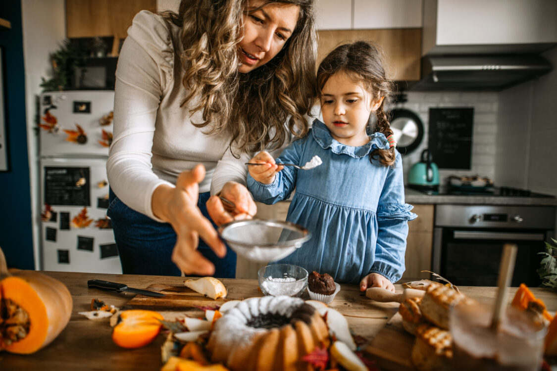 Mère et fille dans la cuisine épousseter le gâteau avec du sucre en poudre
