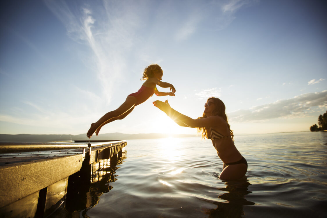 A young girl jumping into her mothers arms in a lake.