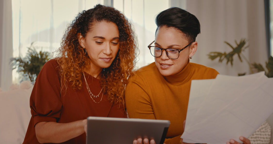 Shot of a young lesbian couple doing paperwork while using a digital tablet at home