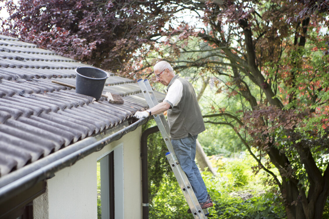 senior man cleaning the gutter of his cottage