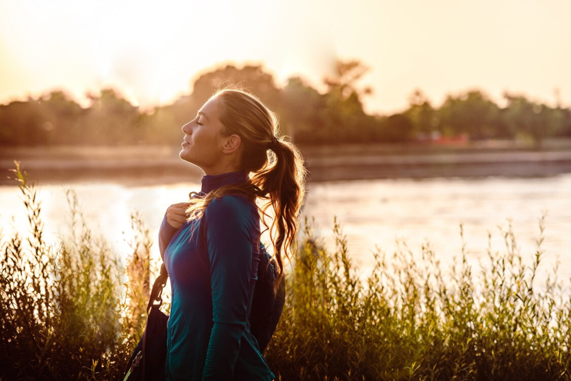 Side view on young woman in sportswear walking by the river and enjoying the sun